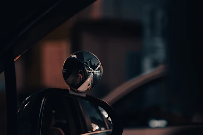 Close-up of a sleek aftermarket side mirror with a glossy black finish reflecting city lights at night.