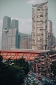 A bustling urban landscape featuring modern high-rise buildings juxtaposed with traditional architecture. An eye-catching red bridge spans across the scene, while a busy street below is filled with cars and vibrant city life.