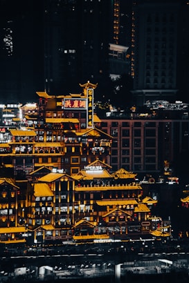 A vibrant cityscape featuring traditional Chinese architecture illuminated with bright yellow and orange lights. The buildings display intricate rooftop designs against a backdrop of modern skyscrapers in the night sky, creating a striking contrast.
