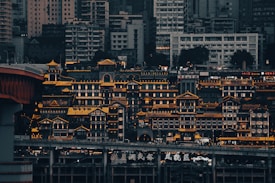 A cityscape featuring an ornate cluster of traditional Chinese-style buildings illuminated with warm lighting, creating a contrast against the dense backdrop of modern high-rise structures. The image captures a blend of traditional architecture and contemporary urban skyline.