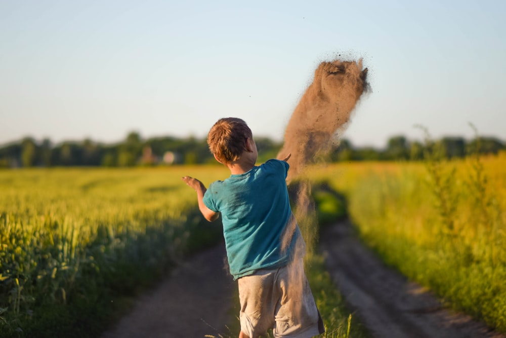 a young boy throwing sand on a dirt road