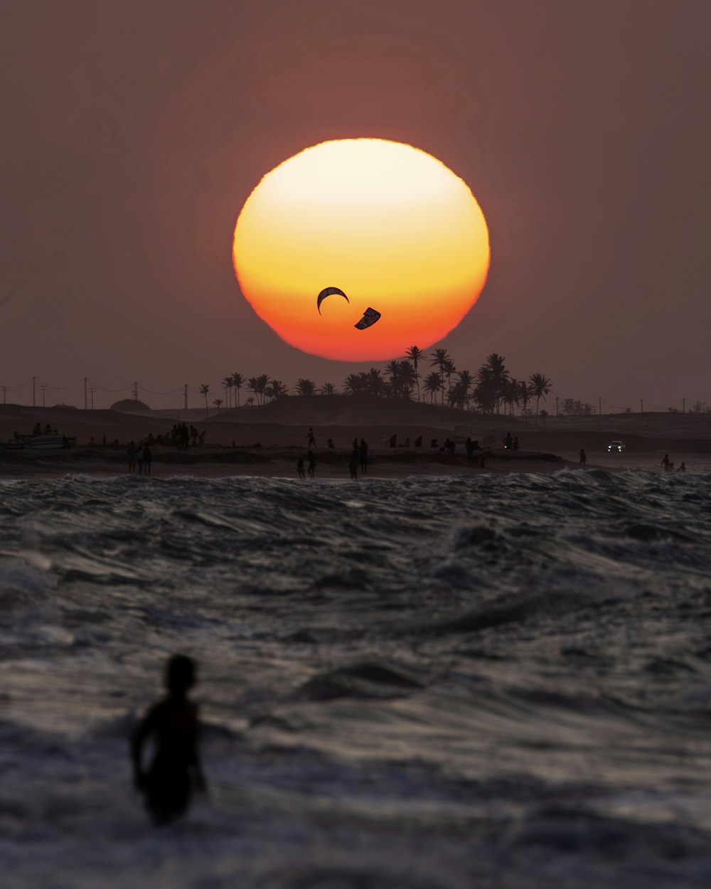 El sol se está poniendo sobre el océano con gente en el agua