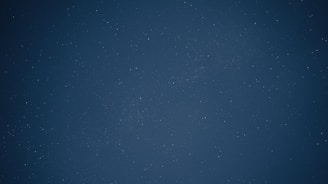 A dark night sky filled with numerous small, faint stars scattered across a deep blue background. The stars appear as tiny dots, creating a mesmerizing and calming cosmic scene.