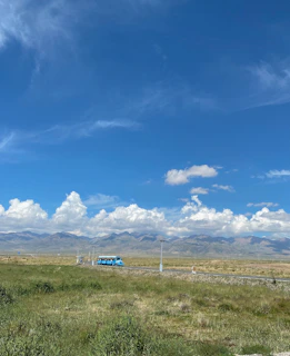 A scenic highway view with a sleek bus cruising past green fields under a clear blue sky.
