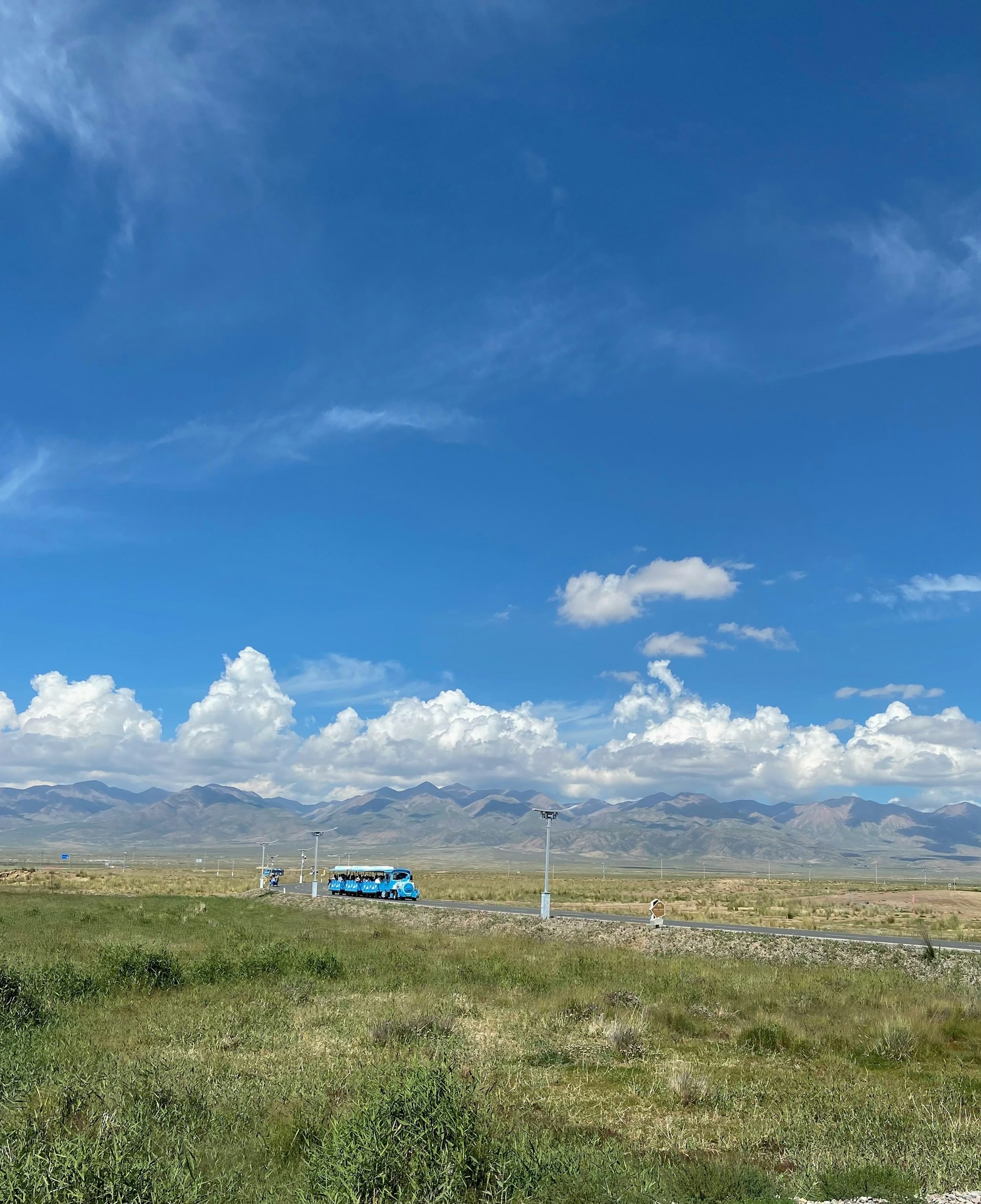 A scenic European countryside with a luxury coach winding through green hills under a bright blue sky.