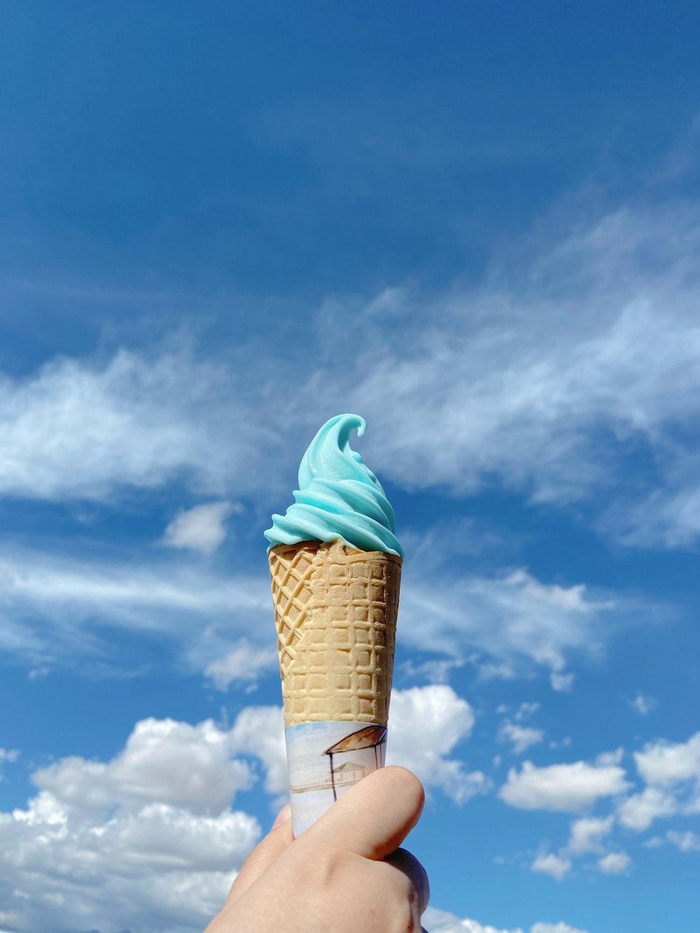 a hand holding an ice cream cone with blue icing