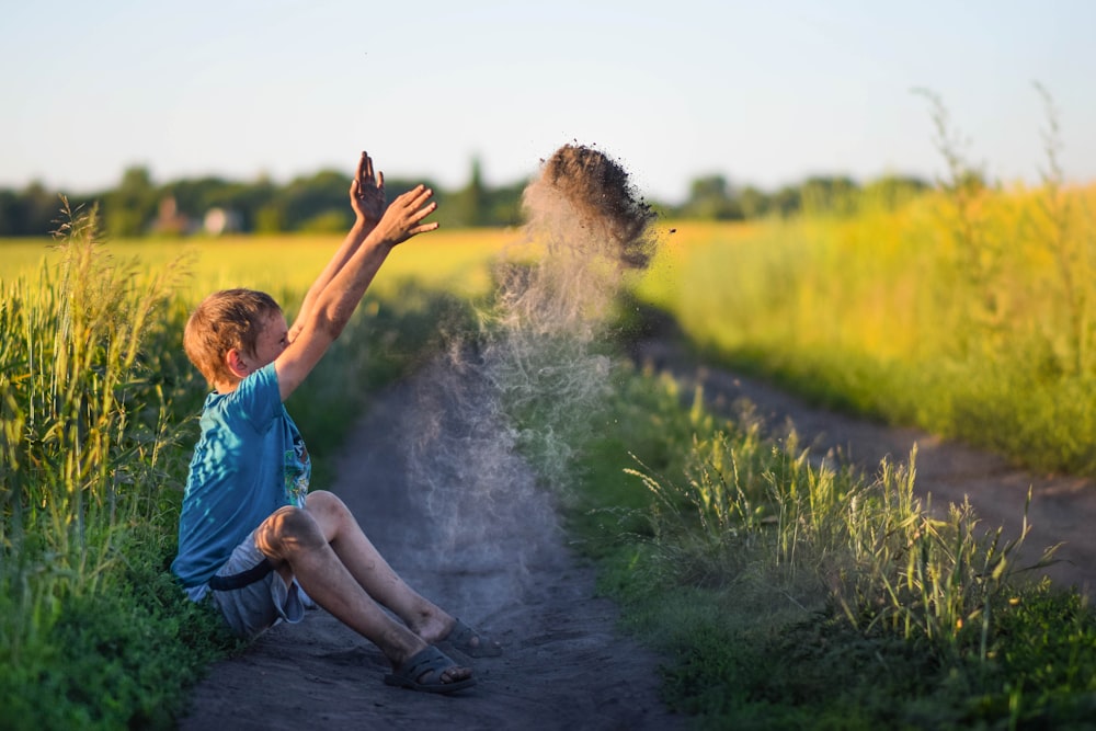 Ein kleiner Junge, der auf einem Feldweg sitzt und Sand in die Luft wirft