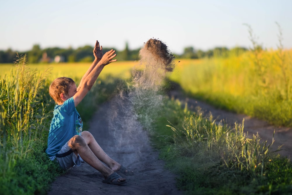 Un niño sentado en un camino de tierra lanzando arena al aire
