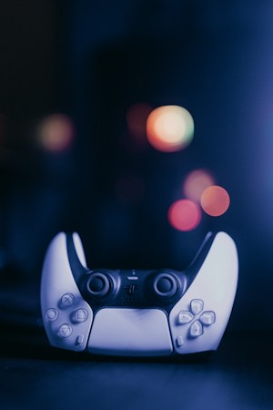 A video game controller with a sleek design is positioned centrally. The background features several out-of-focus, colorful bokeh lights creating a vibrant and slightly futuristic ambiance.
