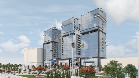 Several modern high-rise buildings with reflective glass facades are surrounded by landscaped areas featuring trees and decorative plants. The buildings are part of a commercial or business complex, and signs such as 'Trading Center' are visible. The sky is clear with a few clouds.