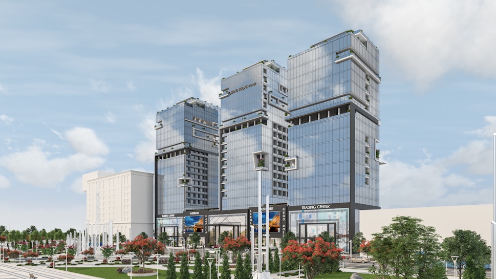 Several modern high-rise buildings with reflective glass facades are surrounded by landscaped areas featuring trees and decorative plants. The buildings are part of a commercial or business complex, and signs such as 'Trading Center' are visible. The sky is clear with a few clouds.
