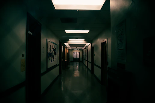 A dimly lit abandoned corridor lined with aged investigation files and scattered photographs, evoking a quiet, investigative atmosphere.