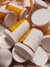Several orange prescription pill bottles are scattered around, each with a white child-resistant cap. The labels are partially visible with text and barcodes, some overlapping each other.