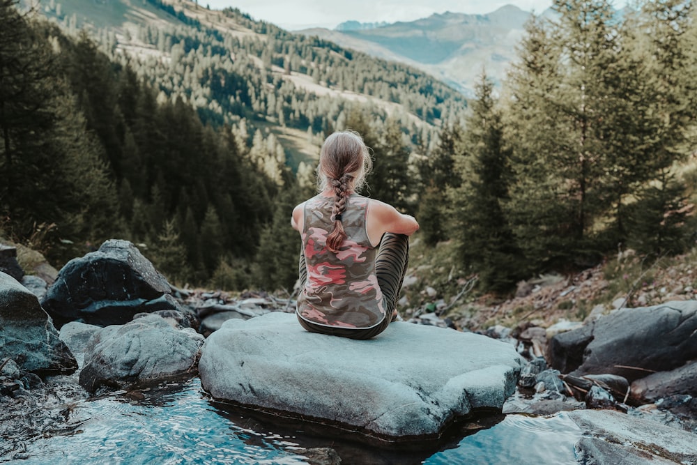 a woman sitting on a rock in the middle of a stream