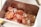 A stainless steel container filled with thinly sliced red grapes. The slices are translucent, showcasing the light and dark red hues with a hint of glossiness from the moisture. The container’s metallic finish reflects the light, adding to the overall brightness of the scene.