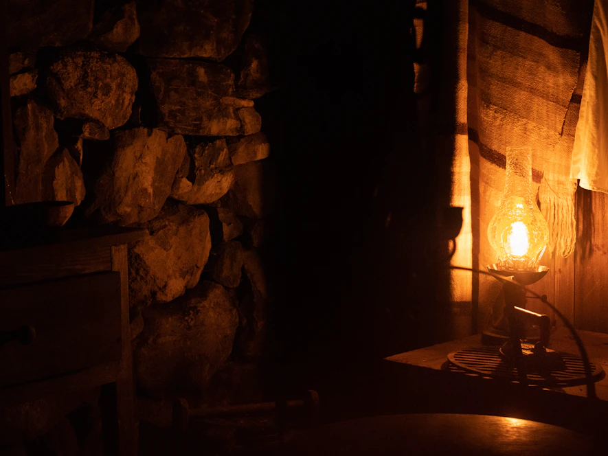 A cozy stone-walled room softly lit by warm amber lights, showcasing minimalist furnishings and rustic textures.