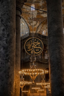 The interior features grand columns and ornate chandeliers, with intricate Islamic calligraphy and detailed mosaic art adorning the walls and dome. The atmosphere is both historic and sacred.
