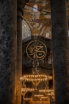 The interior features grand columns and ornate chandeliers, with intricate Islamic calligraphy and detailed mosaic art adorning the walls and dome. The atmosphere is both historic and sacred.