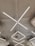 Geometric LED light fixtures are mounted on a white industrial-style ceiling, with an air conditioning unit visible near the center. The lights form intersecting diagonal lines, creating a modern and minimalistic design.