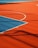 A vibrant sports court with sections of red and blue, featuring crisp white lines marking the boundaries. Shadows from a structure create geometric patterns across the surface, adding depth and interest to the scene.