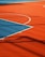 A vibrant sports court with sections of red and blue, featuring crisp white lines marking the boundaries. Shadows from a structure create geometric patterns across the surface, adding depth and interest to the scene.