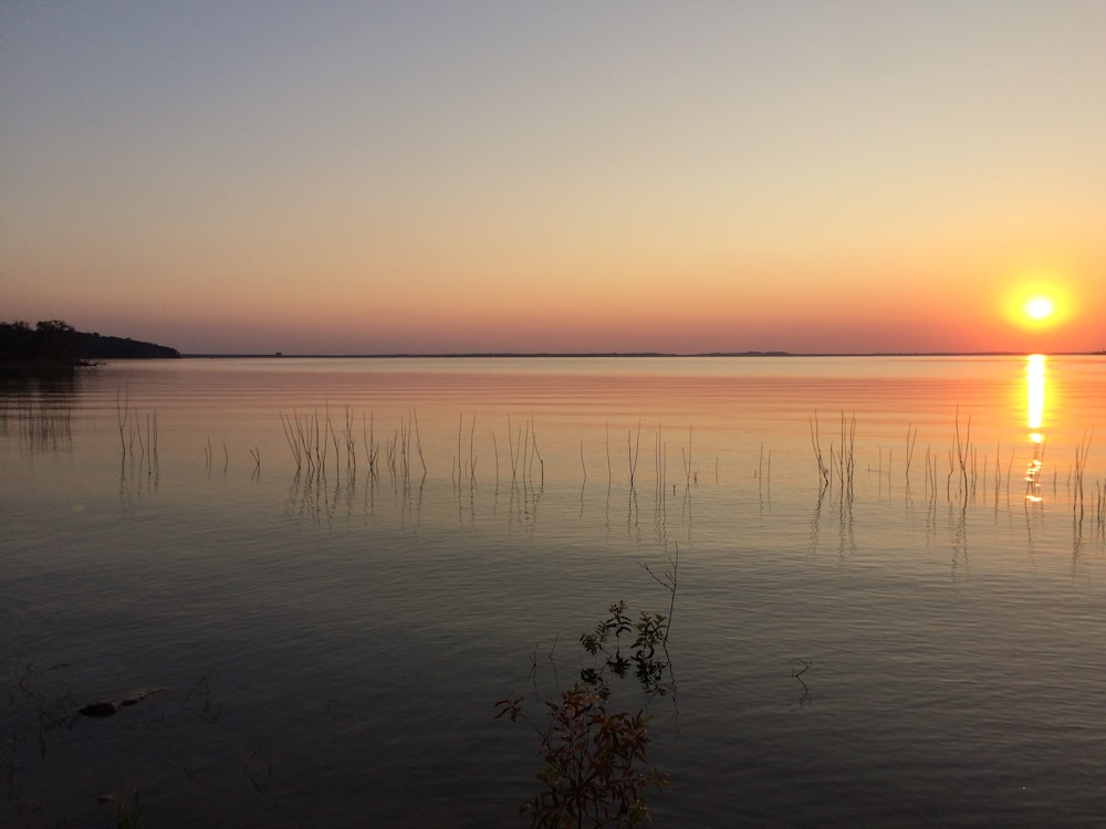 the sun is setting over a calm lake