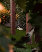 Handcrafted wooden swing hanging in a sunny garden surrounded by flowers.