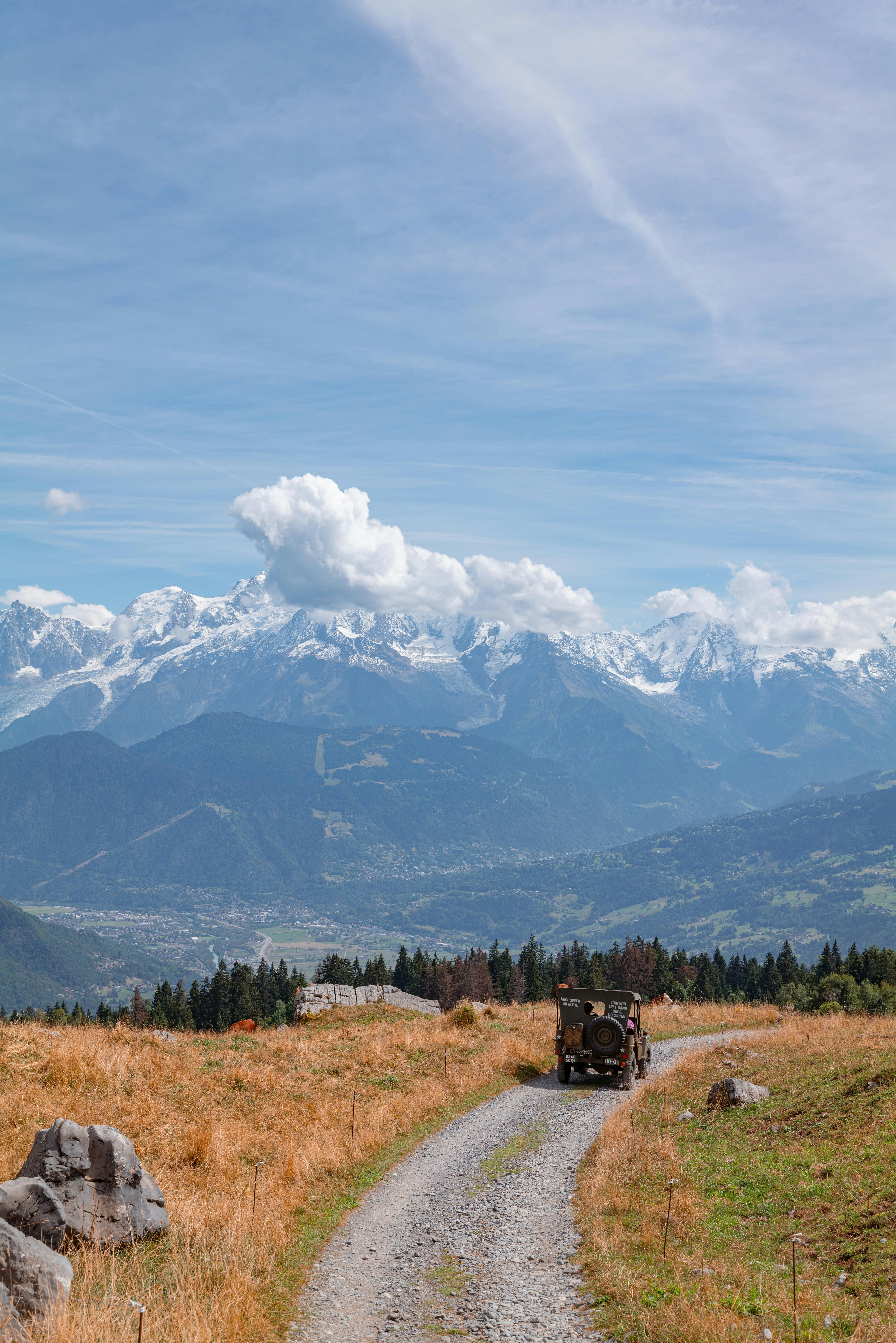 a truck driving down a dirt road in front of a mountain range