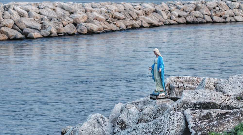 eine Statue einer Person, die auf einem Felsen neben einem Gewässer steht