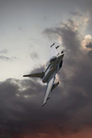 A dynamic shot of a fighter jet flying low over a mountain range at sunset.