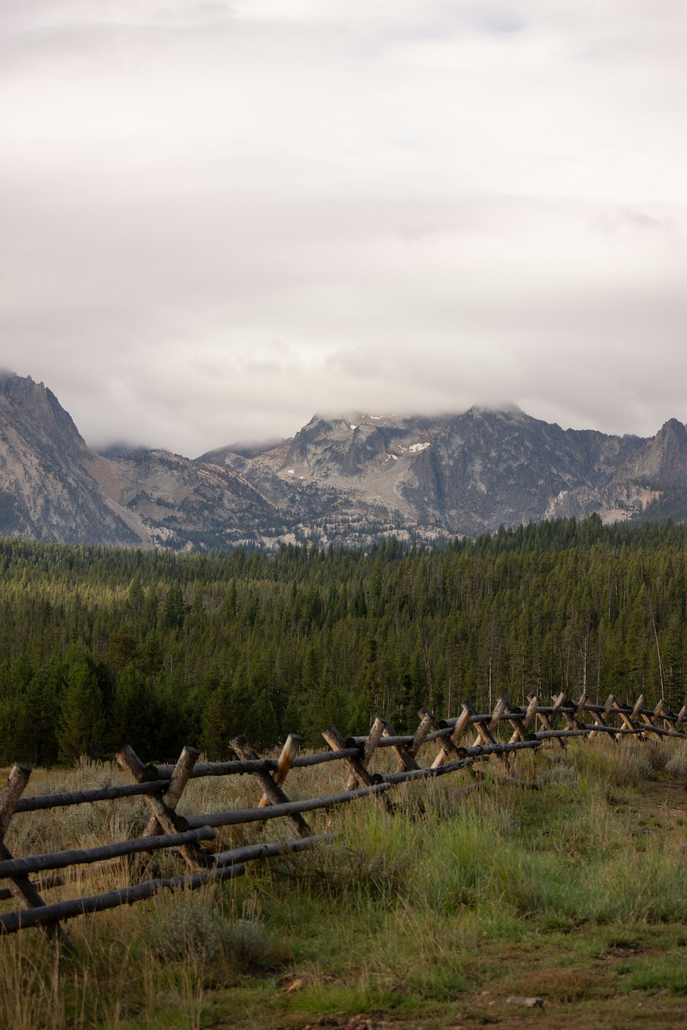 a wooden fence in a field with mountains in the background