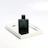 Close-up of a sleek black and gold perfume bottle reflecting soft light on a dark surface.