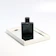 Close-up of a sleek black and gold perfume bottle reflecting soft light on a dark surface.