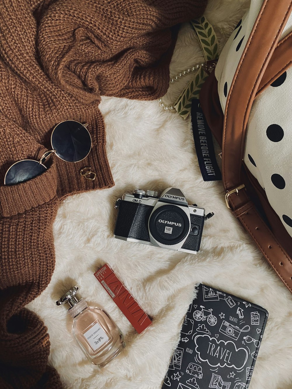 a purse, a camera, sunglasses, and other items laid out on a fur
