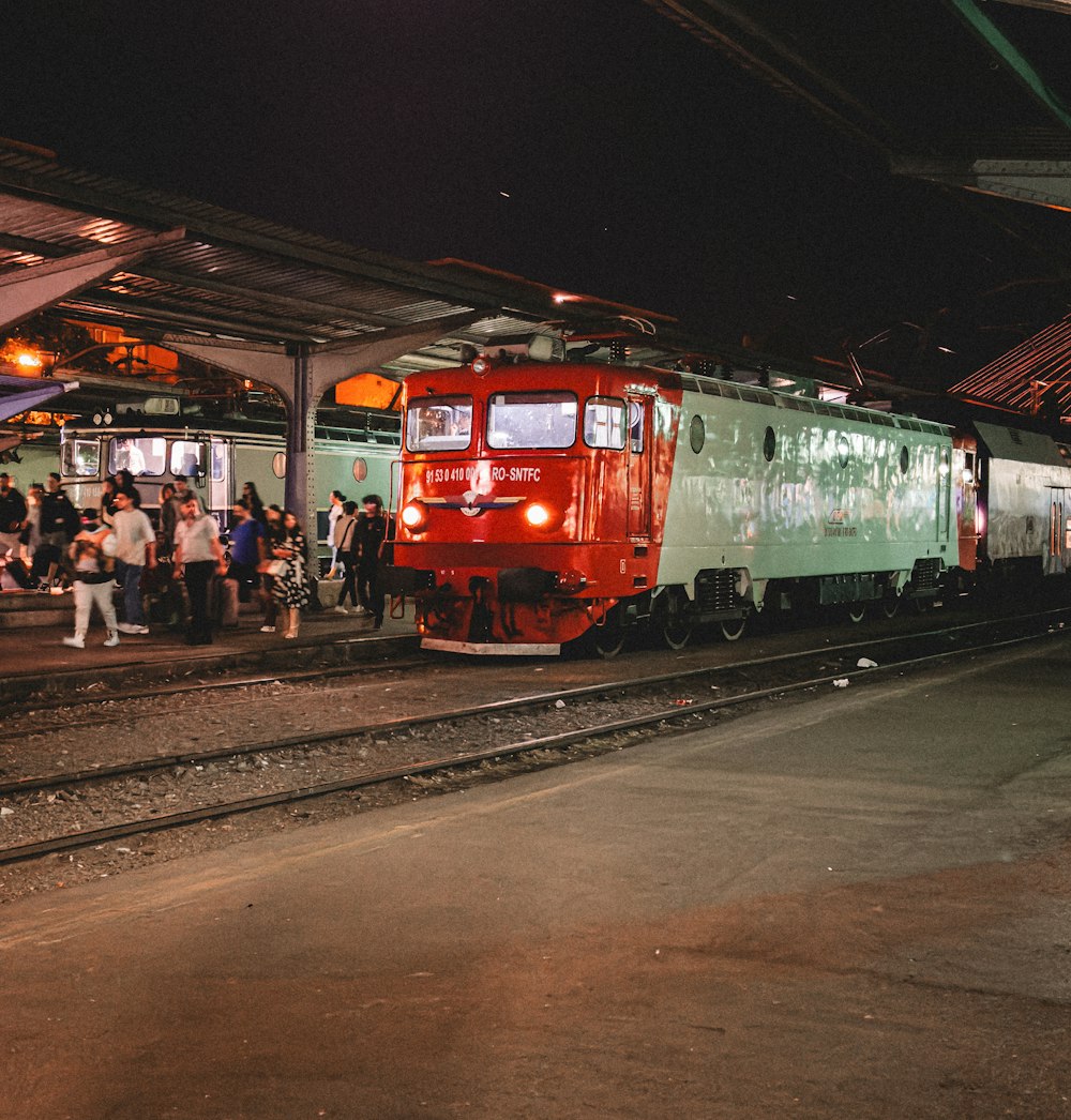 a red and green train pulling into a train station