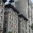 Multiple stories of old, classic style apartment buildings with intricate architectural details. The facades feature large windows and air conditioning units. The brick buildings are a mix of light and dark tones with some greenery visible at the bottom.