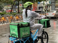 A delivery driver wearing a helmet and gigsecure badge, smiling as they load packages into a bike basket.