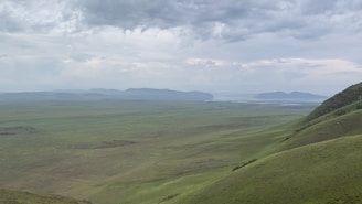 A wide-angle landscape of rolling hills under a dramatic cloudy sky.