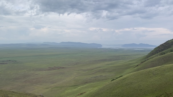 A wide-angle landscape of rolling hills under a dramatic cloudy sky.