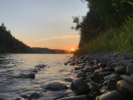 A calm scene showing a peaceful evening sky blending peach and gold hues reflecting on smooth stones and natural skincare products