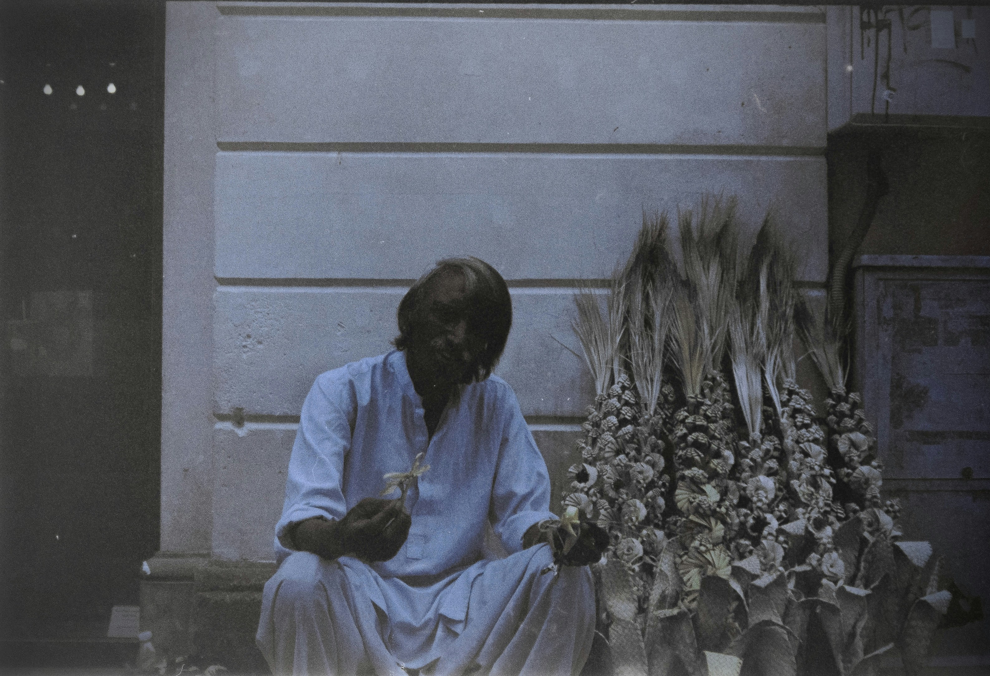 A black and white photo of a young, bespectacled Bengali man, possibly Mani Shankar Mukherjee, sitting at a desk with books and papers.