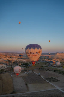 A panoramic shot of multiple hot air balloons floating above rolling hills