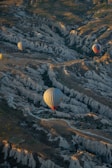 Hot air balloons float gracefully over a rugged terrain of deep valleys and unique rock formations with the soft light of either sunrise or sunset casting warm hues across the landscape.