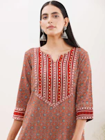A festive kurti with intricate patterns in gold thread, styled with matching accessories on a minimalist stand.