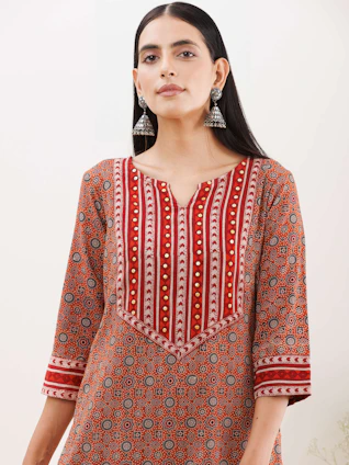 A vibrant kurti displayed on a wooden hanger against a rustic textile backdrop, highlighting intricate patterns.