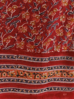 A vibrant red fabric featuring intricate floral patterns. The flowers are primarily yellow, white, and orange, with green leaves. The design includes parallel bands with floral motifs that stretch horizontally across the fabric.