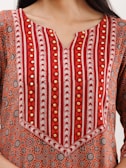 A close-up of a garment with intricate patterns featuring red, orange, and white stripes, along with circular geometric motifs. The fabric is embellished with gold-colored decorative elements.