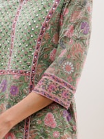 A detailed, close-up view of a garment with intricate floral patterns in shades of green, pink, and purple. The fabric features embellished details and a luxurious texture, suggesting a traditional or cultural style.