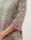 A detailed, close-up view of a garment with intricate floral patterns in shades of green, pink, and purple. The fabric features embellished details and a luxurious texture, suggesting a traditional or cultural style.