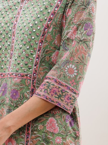 A detailed, close-up view of a garment with intricate floral patterns in shades of green, pink, and purple. The fabric features embellished details and a luxurious texture, suggesting a traditional or cultural style.